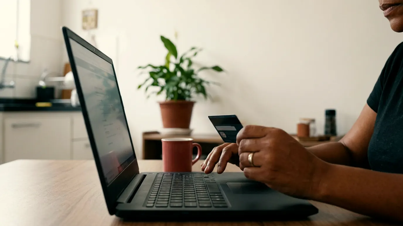 Mãos pagando uma conta no notebook com o cartão, com um calendário na parede