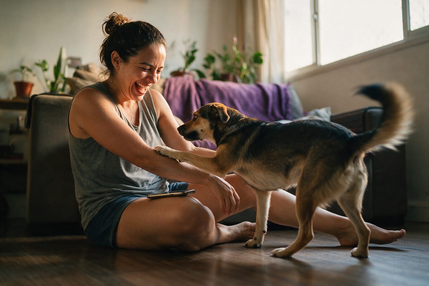 Tutora rindo no chão da sala enquanto o cachorro põe a pata no braço dela